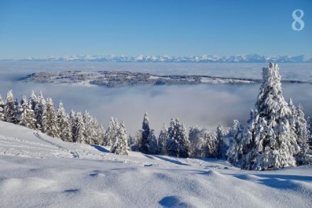 Paesaggio innevato sopra uno strato di nebbia alta.