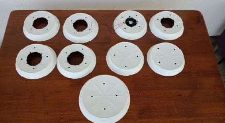 Figura 2: tutti i sottovasi sono pitturati di bianco all'esterno. Cinque sottovasi da 20 cm di diametro hanno un foro di 8 cm al centro e uno ha un foro centrale leggermente più piccolo per facilitare l'installazione della ventola (facoltativa). Si può notare che il ritaglio del foro non è molto preciso, questo è dovuto alla mancanza di strumenti adeguati per eseguire il lavoro.
