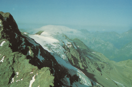 Figura 3: Nube (di tipo “pileus”) sulla cima del Pizzo Corciusa, in Val Mesolcina, vista da est verso ovest il 30 luglio 1993 alle 10. Questa nube indica un peggioramento del tempo, preannunciato anche dalla foschia che penetra dalla pianura Padana verso le Alpi (da sinistra verso destra). Davanti ad un fronte temporalesco che sopraggiungerà la sera, in arrivo da ovest, l’aumento dell’umidità dell’aria favorisce la formazione di tale nube, che normalmente scompare prima dell’inizio del vero e proprio peggioramento. 