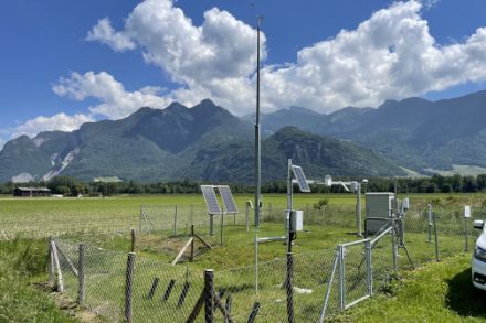 Stazione meteorologica in un campo con le montagne sullo sfondo.