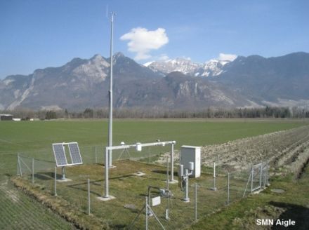 Immagine di una stazione meteorologica recintata con gli strumenti di misurazione su un prato verde. 