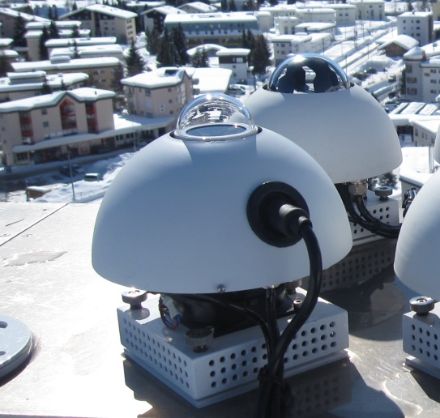 Due biometri UV con una piccola cupola di vetro e una copertura sferica che protegge gli strumenti dagli agenti atmosferici. Sullo sfondo le case innevate di Davos.