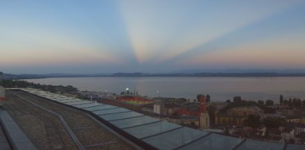 Vista su un lago, con i raggi del Sole al tramonto che si diffondono verso l’alto e scompaiono all'orizzonte.