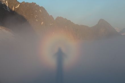 Immagine di un paesaggio di montagna in cui in primo piano si possono osservare nella nebbia gli anelli colorati e l’ombra della persona che ha scattato la fotografia.