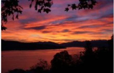 In primo piano il lago di Zurigo con cielo arancione e rosso per effetto di banchi nuvolosi.
