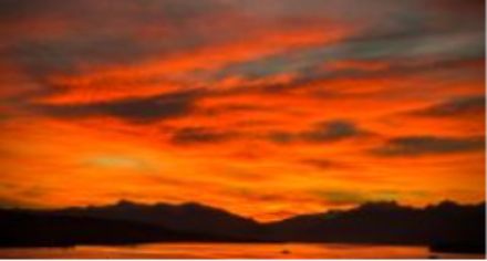 Alba colorata su un lago con montagne sullo sfondo.