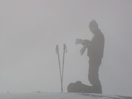 Immagine di uno sci escursionista nella nebbia, che sta consultando una carta geografica.