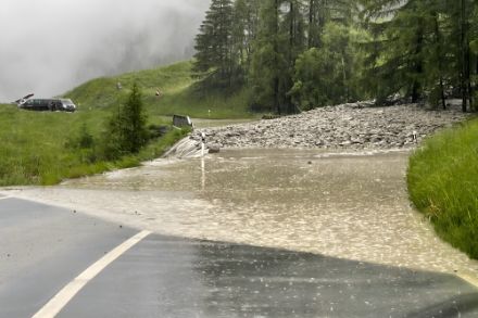 Una strada di montagna allagata a causa delle forti piogge, l'acqua copre la carreggiata e la rende impraticabile.