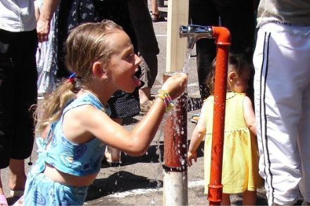 Una ragazza si rinfresca a un rubinetto pubblico