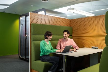 due collaboratori di MeteoSvizzera, una donna e un uomo, sono seduti in una cabina per riunioni verde con un tavolo negli uffici di MeteoSvizzera e lavorano assieme con un computer portatile. Sul tavolo ci sono anche due telefoni cellulari.